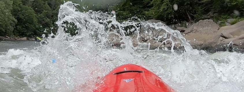 Water splashing on a red kayak going down a rapid.